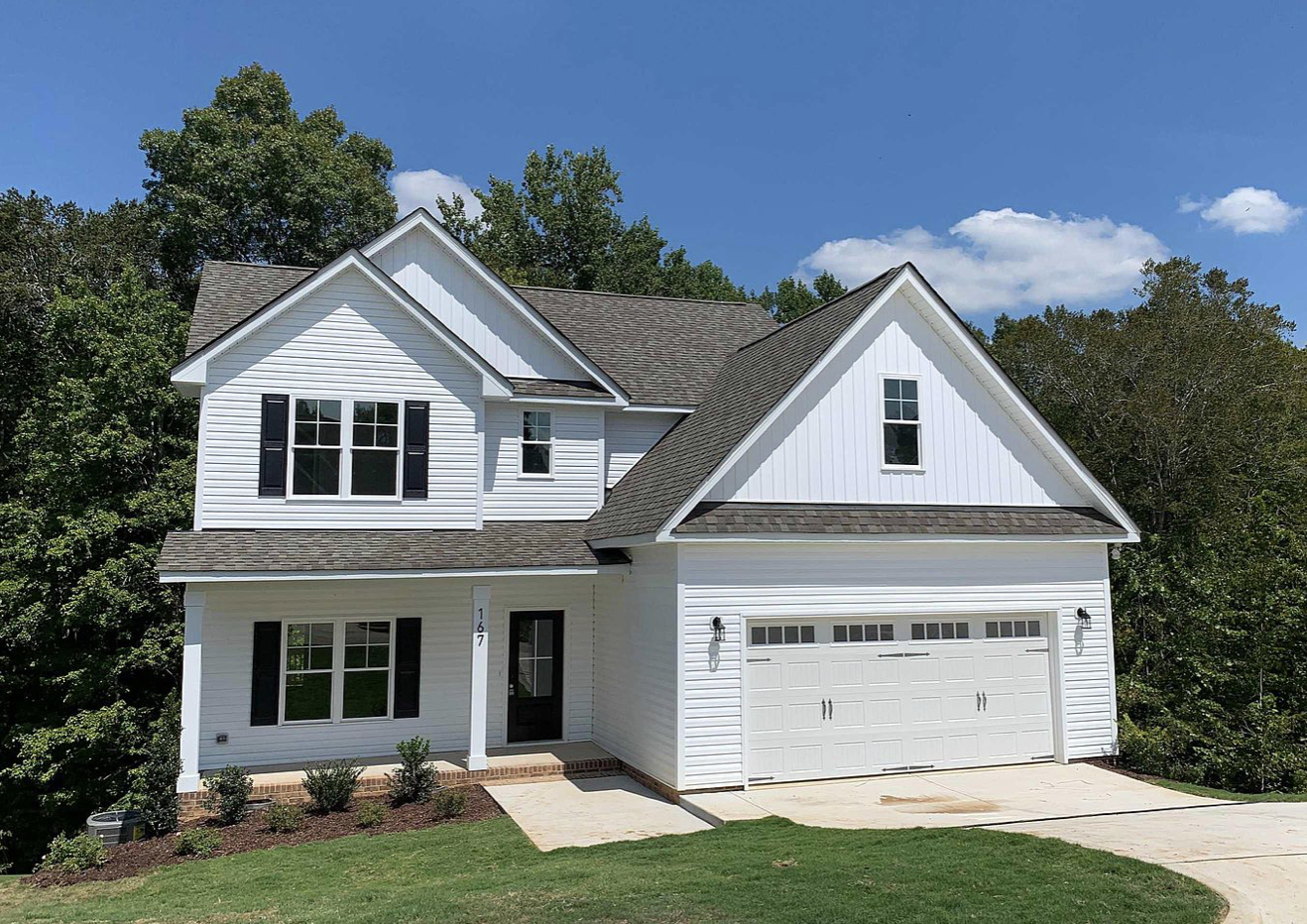 A white house with a garage door and trees in the background.