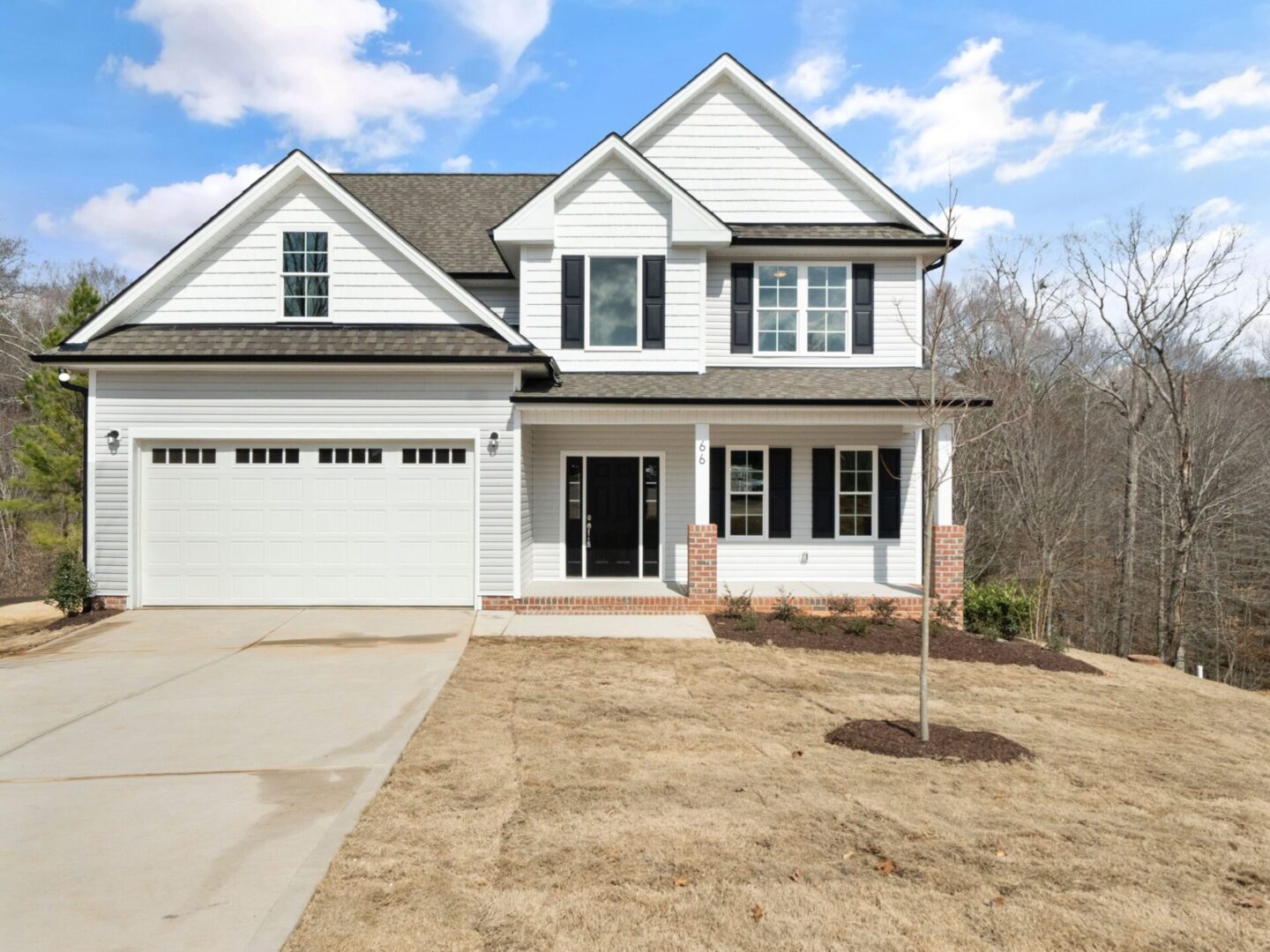 A white house with a driveway and trees in the background.